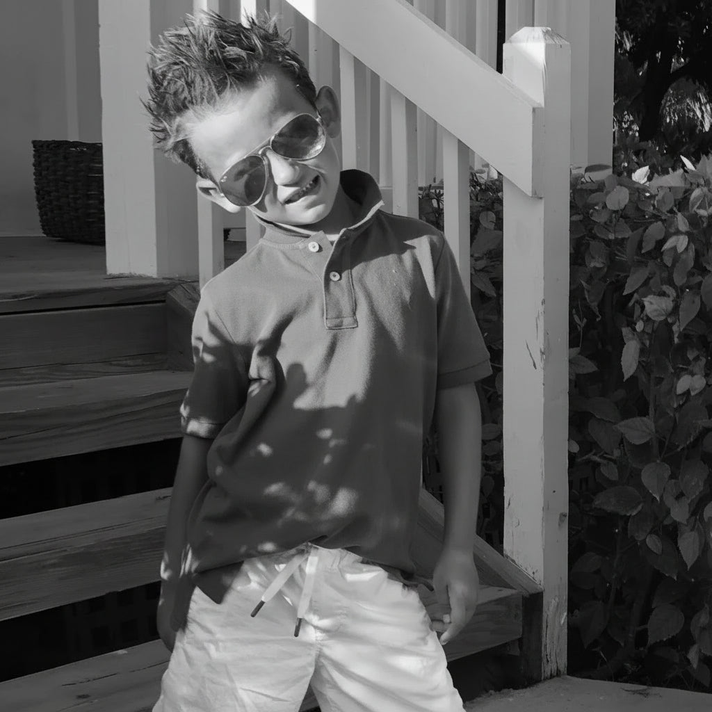 Child wearing a blue polo shirt and reflective sunglasses outdoors.